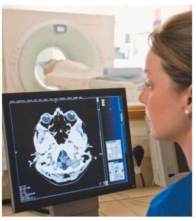 Hình 38.9: Bác sĩ chẩn đoán hình ảnh đang điều khiển máy quét chụp cắt lớp vi tính (CT scanner, quan sát qua cửa kính chắn xạ) từ phòng điều khiển cách ly nhằm tránh phơi nhiễm tia X lặp lại nhiều lần.